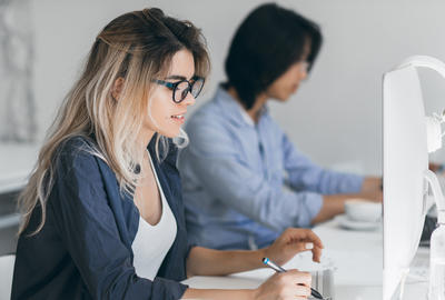 Busy female freelancer with long hair working with tablet and drinking coffee